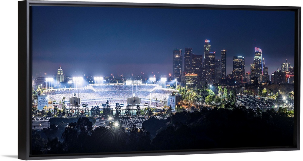 Photograph of Dodger Stadium lit up on a game night with the Los Angeles skyline on the right.