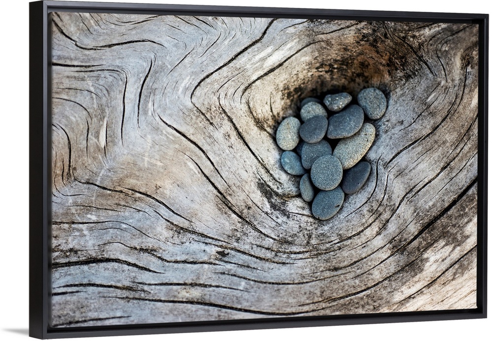 Photograph of smooth rocks piled on top of a piece of driftwood on the pacific northwest coast.