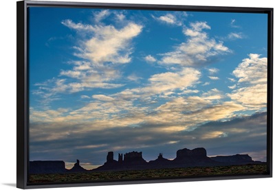 Fluffy Clouds Drift Over A Silhouette Of Rock Formations In Monument Valley, Utah
