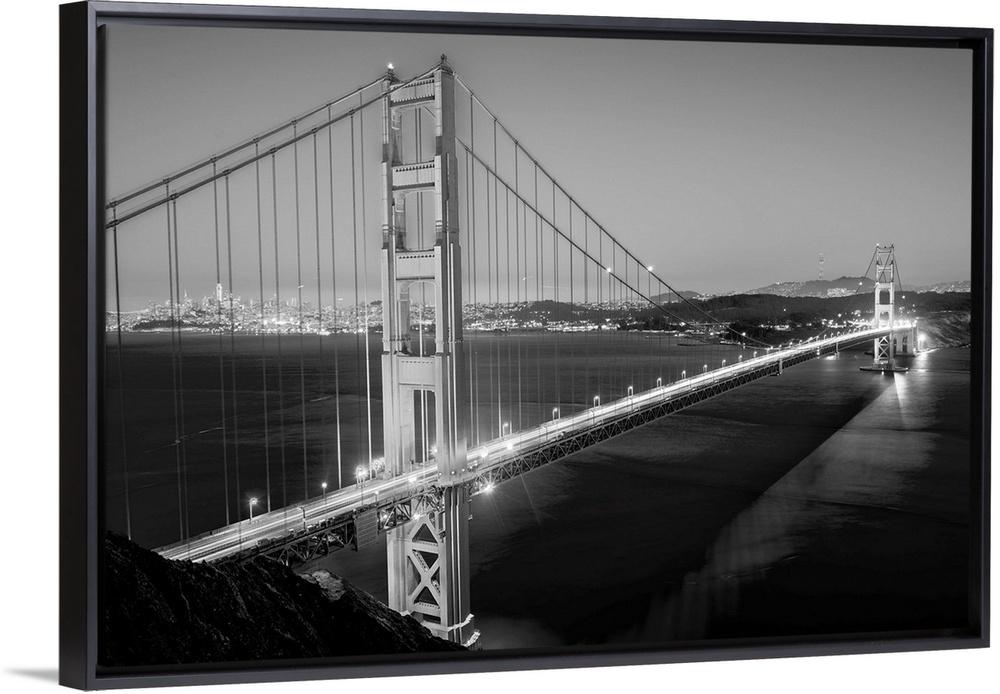 Cool toned photograph of the Golden Gate Bridge lit up at twilight with the city lights in the background.