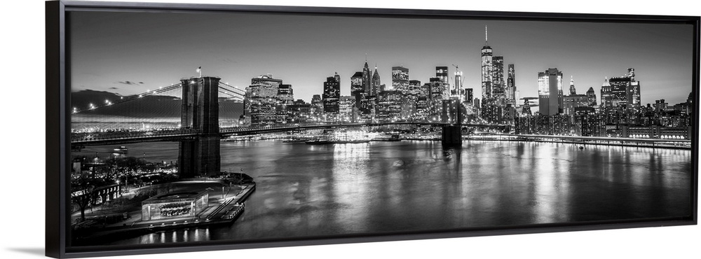 View of the New York City skyline illuminated at night, with the Brooklyn Bridge, from across the water.