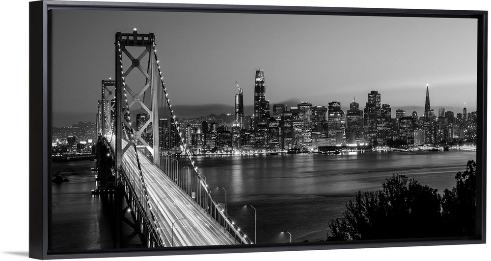 Photograph of the Bay Bridge with a sunset and the San Francisco skyline lit up in the background.