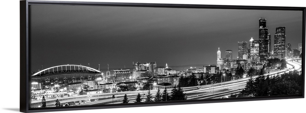 Panoramic photograph of the Seattle skyline with the stadium on the left and light trails from traffic on the highway.