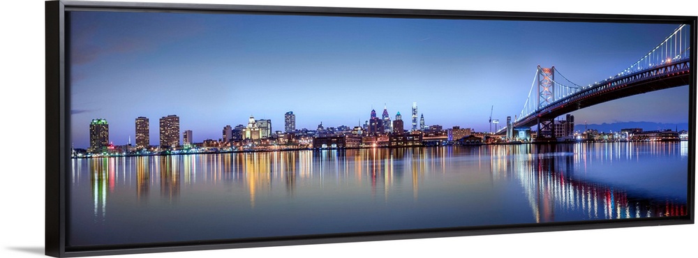 Panoramic photo of the Philadelphia city skyline reflected in the water at night, with the Benjamin Franklin Bridge on the...