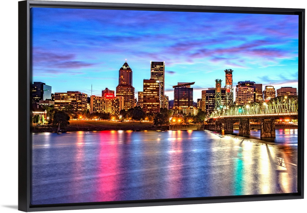 Photograph of the Portland, Oregon skyline lit up at sunset with colors reflecting onto the Willamette River in the foregr...