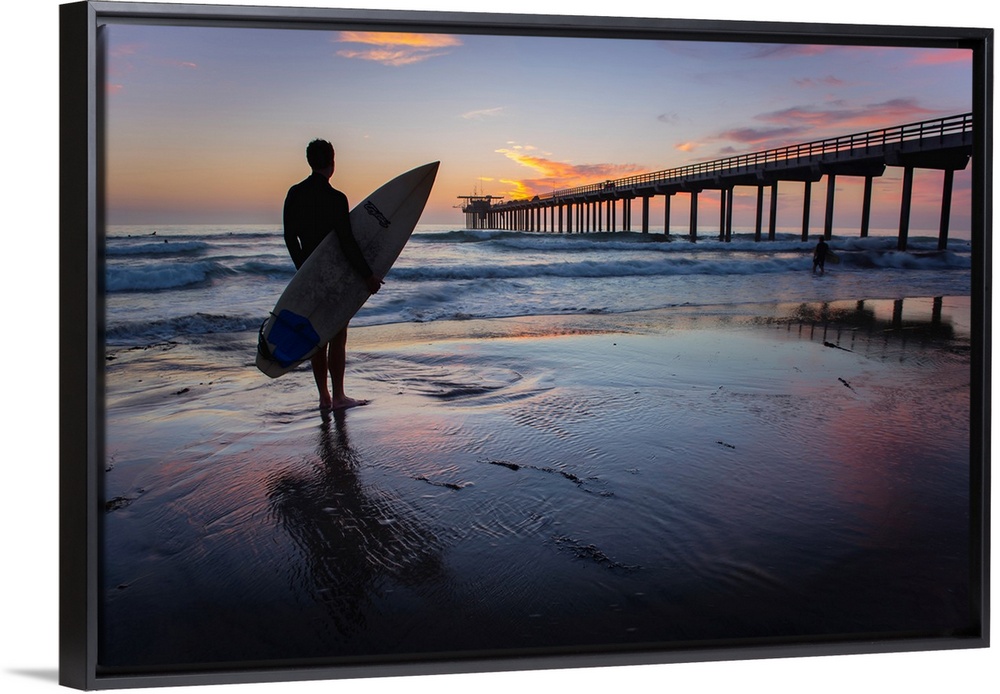Silhouetted photograph of a man holding a surf board on the shore of Ocean Beach in San Diego, California, with the Ocean ...