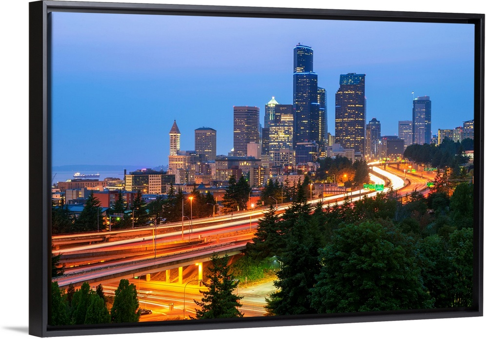 Photograph of the Seattle skyline at dusk with light trails from the cars on the highway in the foreground.