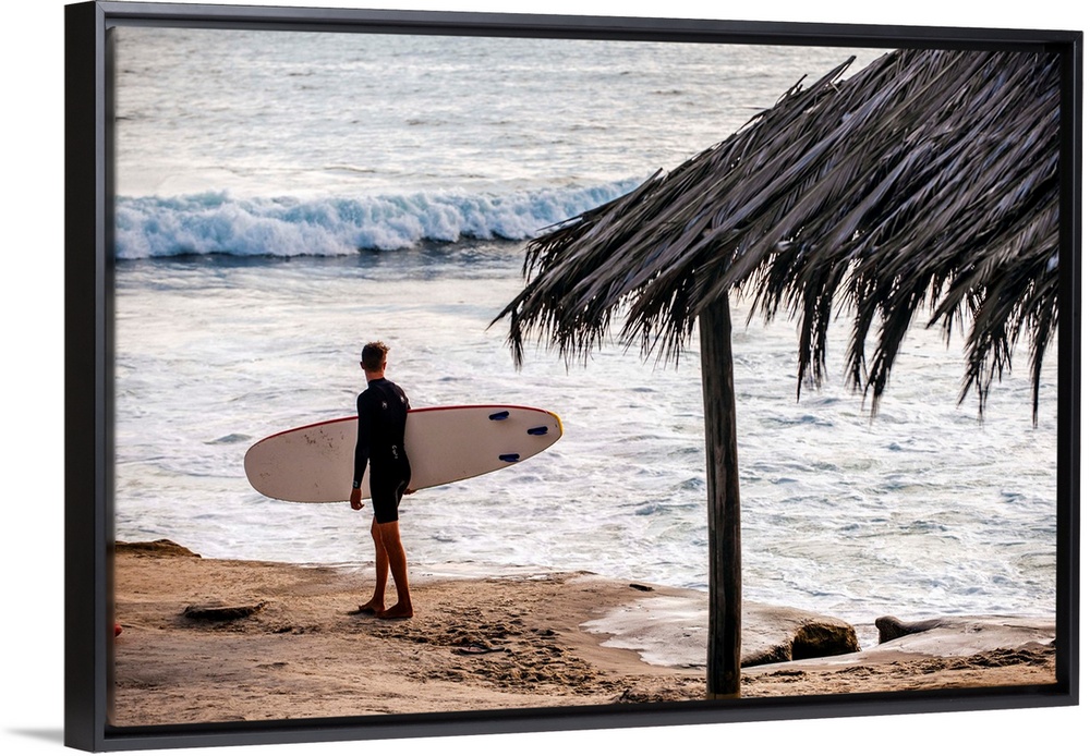 Photograph of a surfer walking along the shore of the pacific ocean in San Diego, California, with a cabana built with nat...