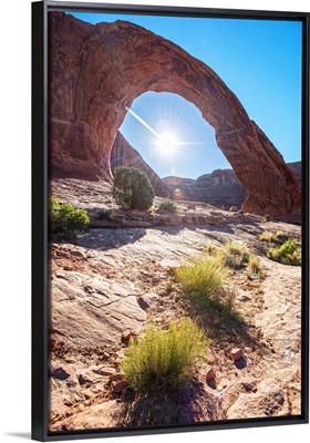 The sun shining behind the Corona Arch in Arches National Park, Utah