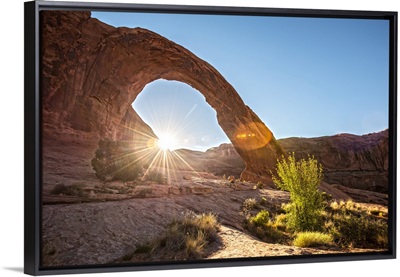 The sun shining behind the Corona Arch in Arches National Park, Utah