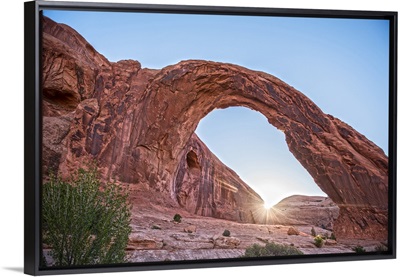 The sun shining on the horizon behind the Corona Arch, Arches National Park, Utah.