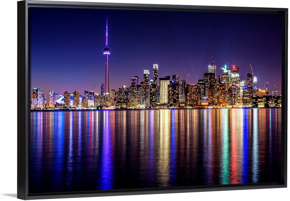 Photo of the Toronto city skyline with lights reflected in the water at night.