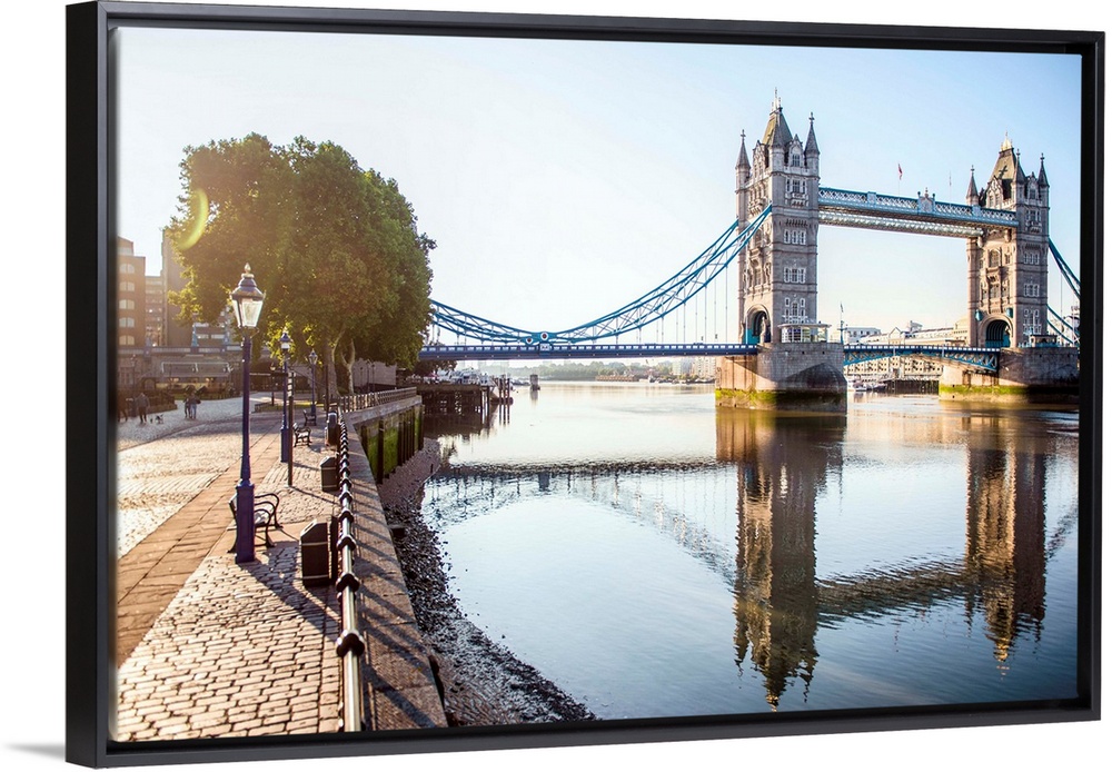 Photograph of Tower Bridge  reflecting on River Thames with a brick sidewalk on the side.