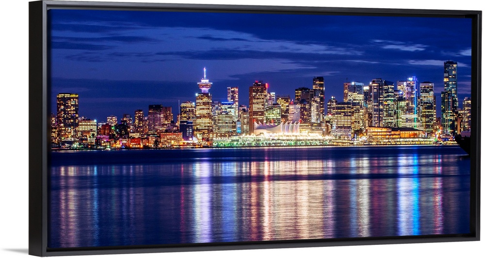 Photograph of the Vancouver, British Columbia skyline lit up on a dark blue night and reflecting bands of colorful light o...