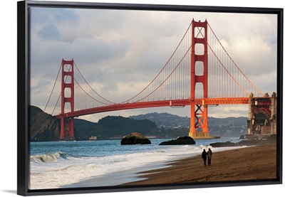A couple strolling on Baker Beach near the Golden Gate Bridge at dawn