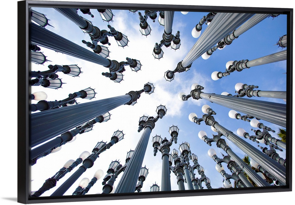 Big photograph taken from the ground looking up focuses on an art display incorporating vast amounts of light posts set in...