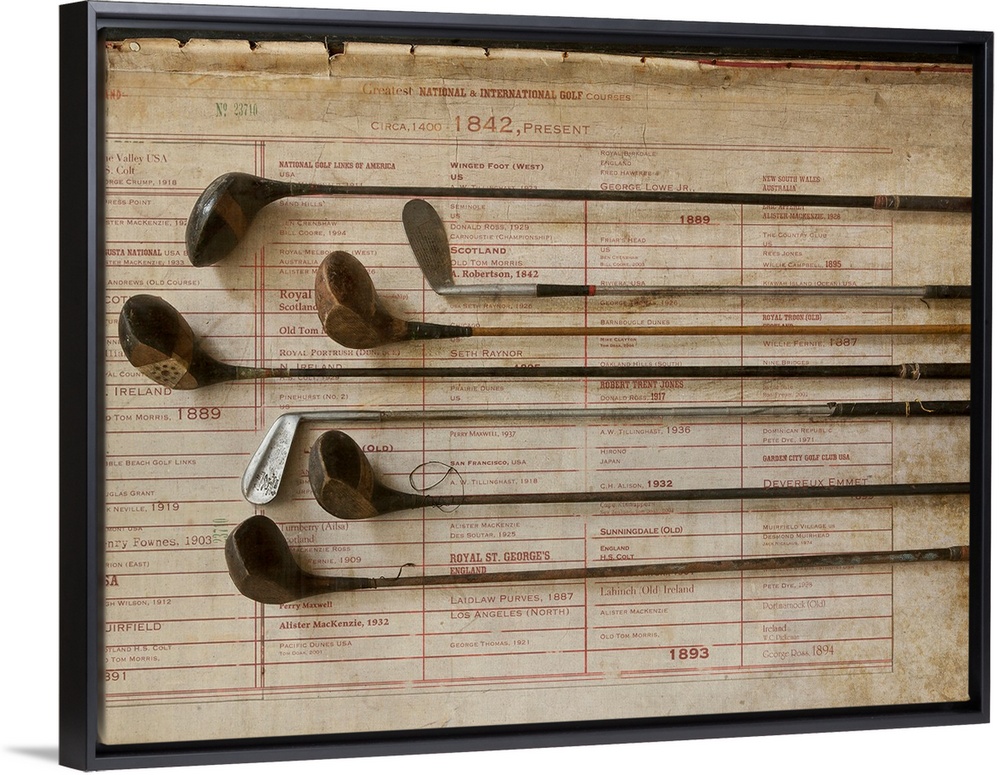 Antique golf clubs are lined up and lay over a vintage poster of major golf tournaments.