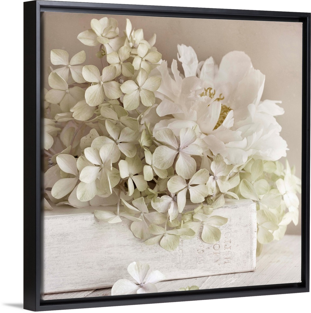 Square photo on canvas of white flowers laying on top of a white book with the spine facing the camera.