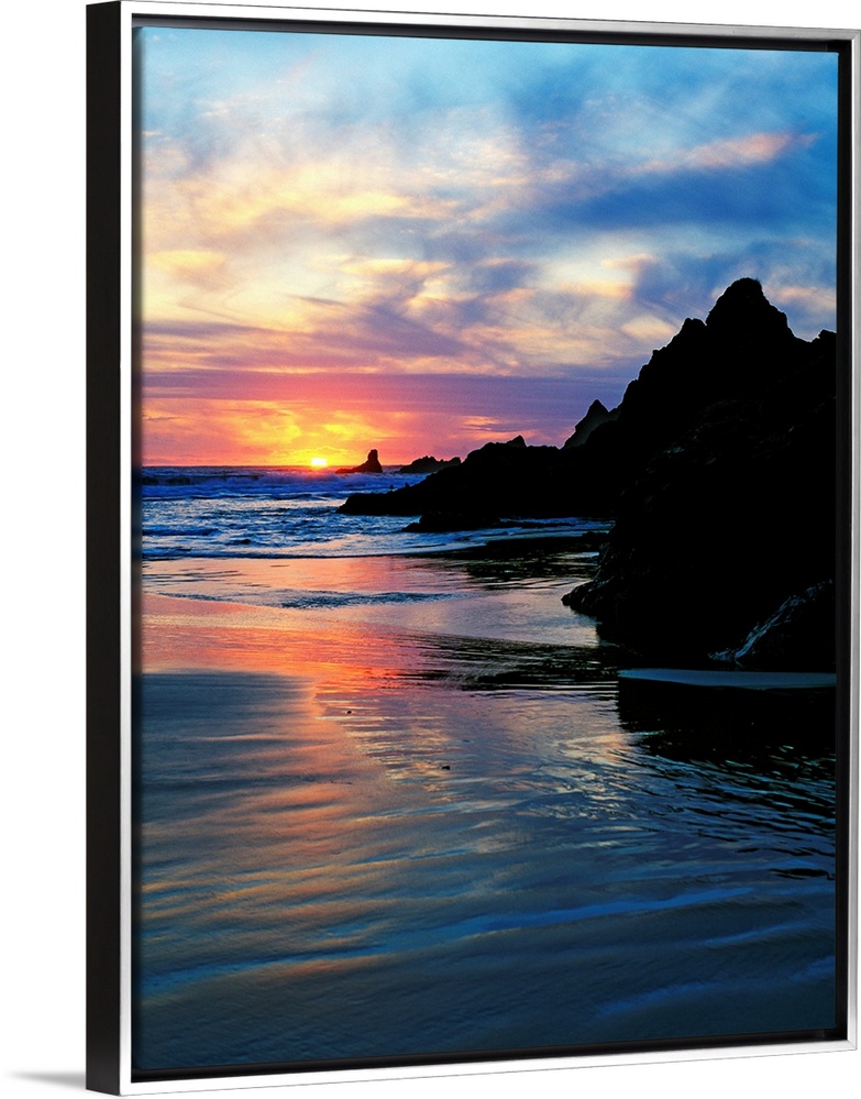 Sun below the horizon in a seascape with a rocky beach and waves.