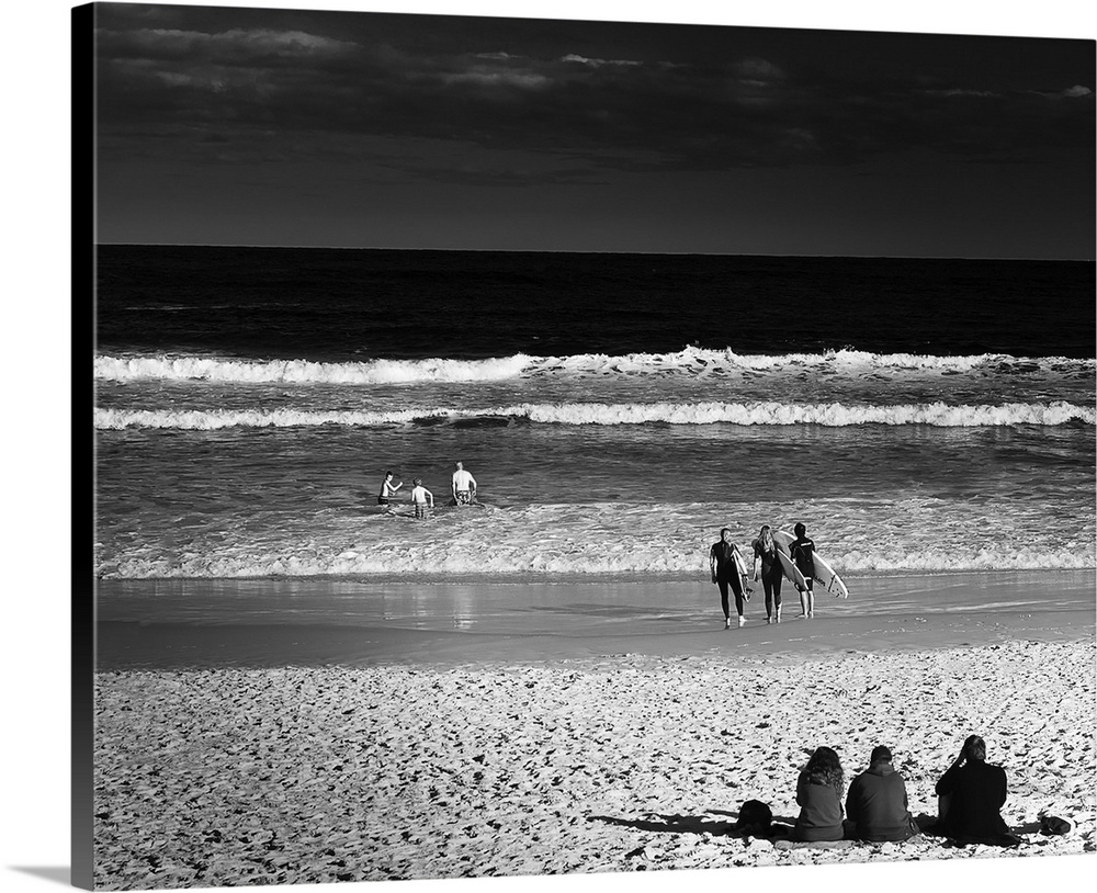 Square black and white photograph of people in groups of 3 enjoying the beach in different ways, Australia.