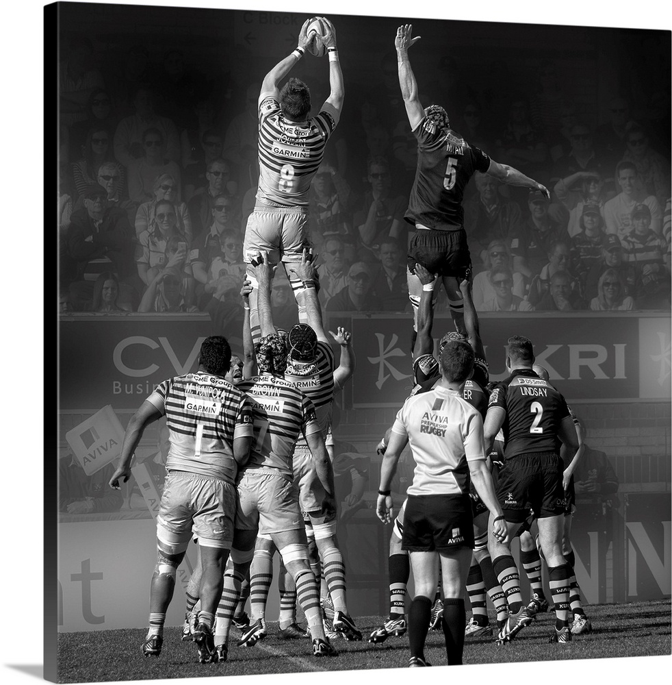 A black and white photograph of rugby players in a match reaching into air to grasp the ball.
