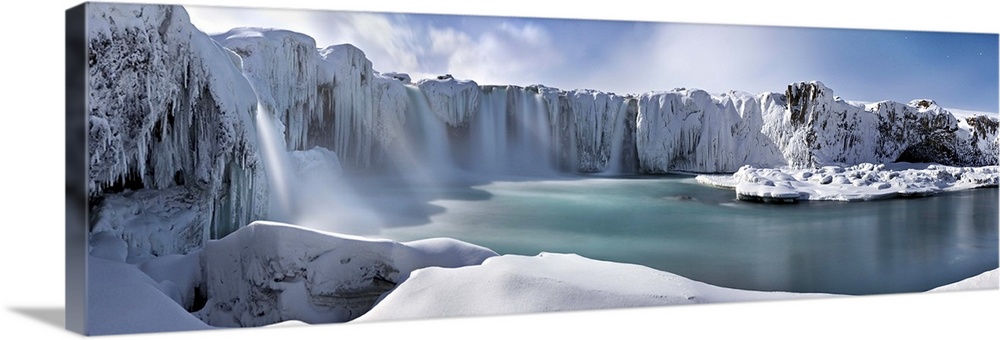 Icy snow covered landscape with waterfalls streaming down from cliffs surrounding a river.