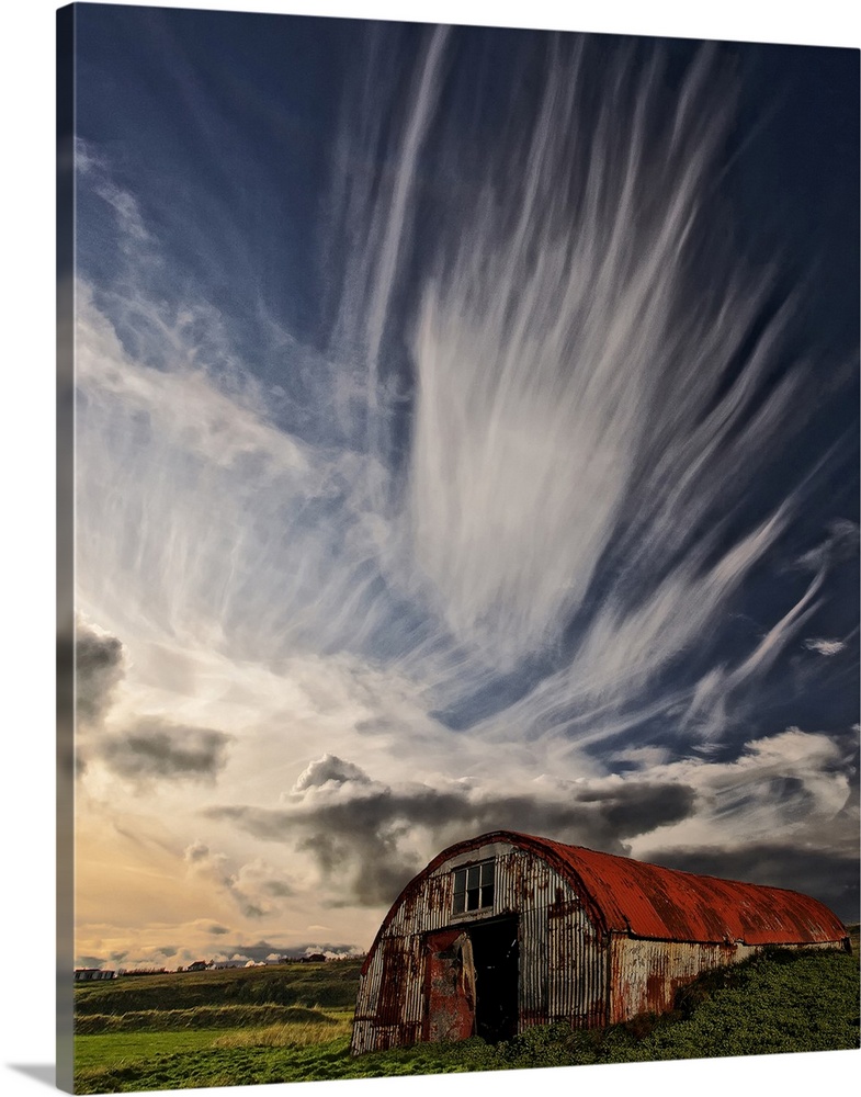 A rusty dilapidated building in a green field under a sky filled with dramatic clouds, Iceland.