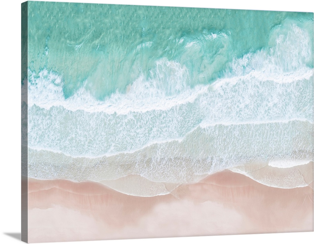 An artistic overhead photograph of turquoise waves lapping onto a pink sandy beach. The colors in the image are light fres...