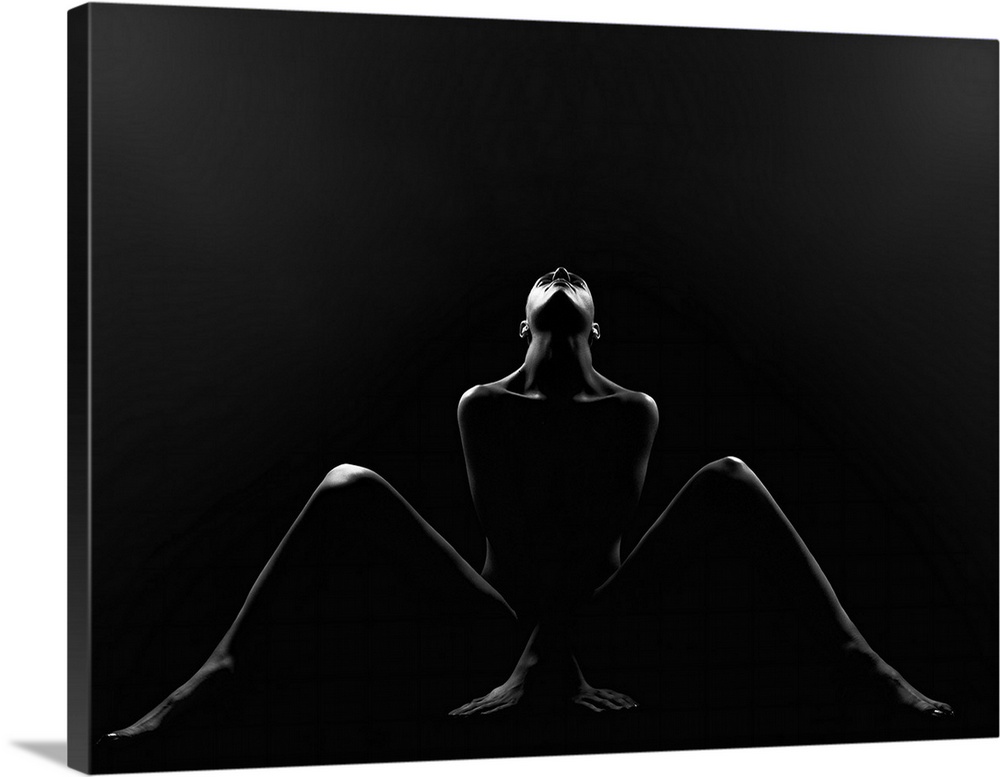 Low key black and white fine art photograph of a silhouette of a woman sitting on the ground, looking up, with her legs sp...