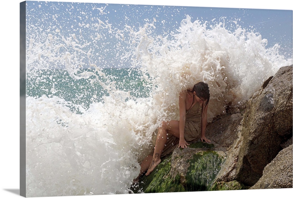 A model on ocean rocks braces herself against the crashing waves.