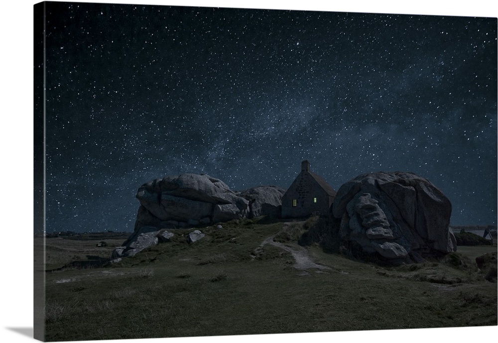 A small house nestled between large rock formations under a night sky full of stars.