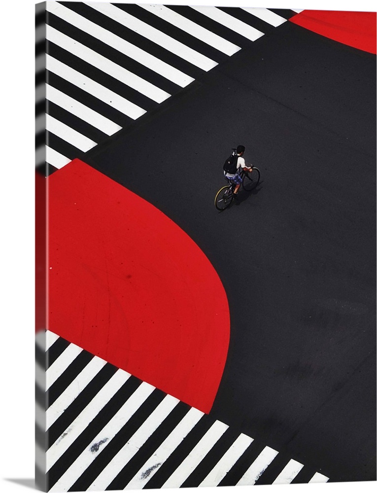 A cyclist crossing the center of a street painted with zebra crossings and red lanes.