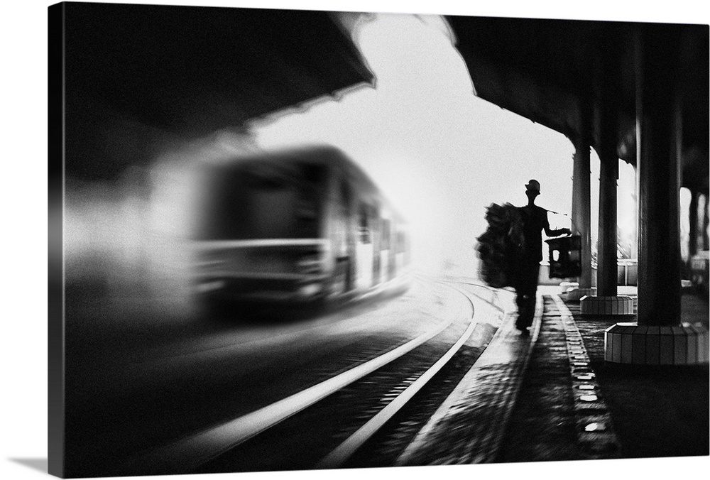 A man with luggage walks along a train station platform with a train on the rails nearby, Jakarta.