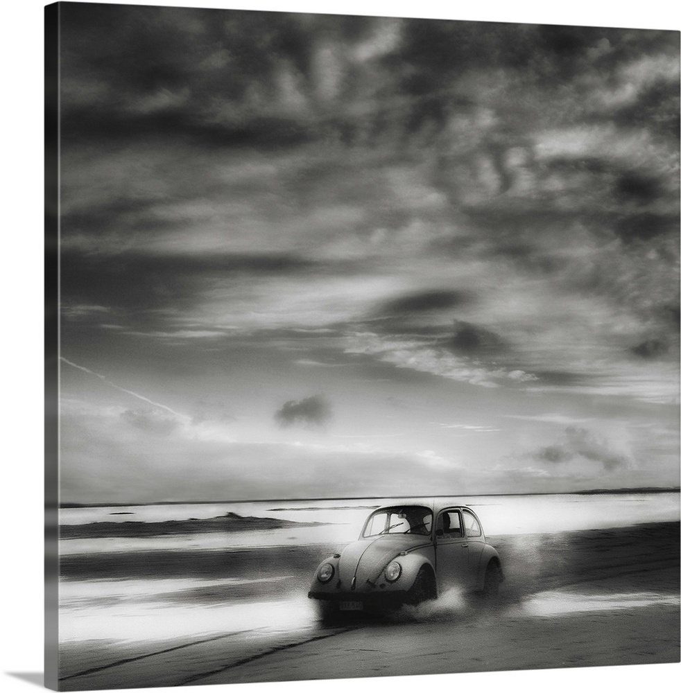 A Volkswagen Beetle driving down a sandy beach with stunning clouds overhead.