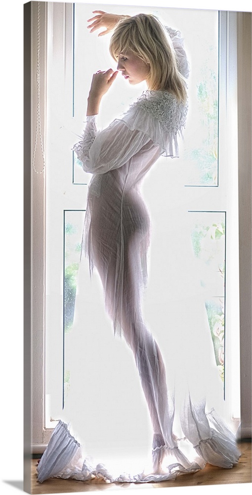 Portrait of a beautiful young woman in a sheer nightgown standing in front of a window.