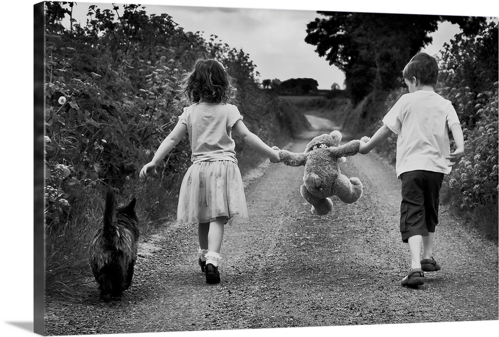 A young boy and girl each holding the arm of a teddy bear walk with their dog along a path.