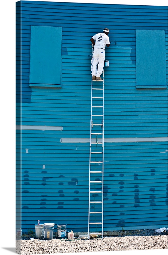A painter high on a ladder refinishes blue siding on a building, Charleston, South Carolina.
