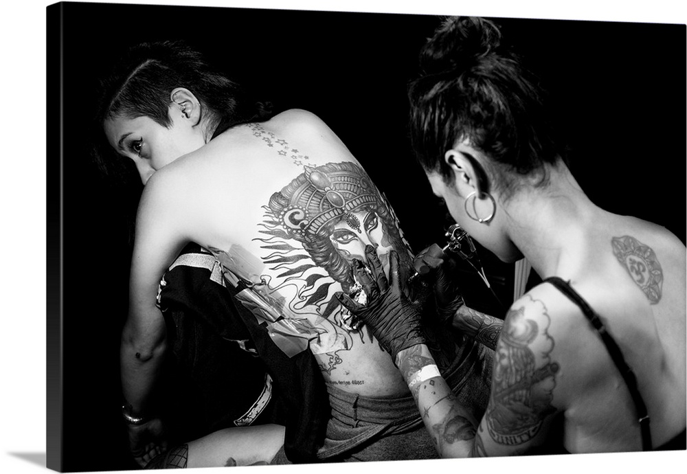 A lady tattooist working on a backpiece on another woman.