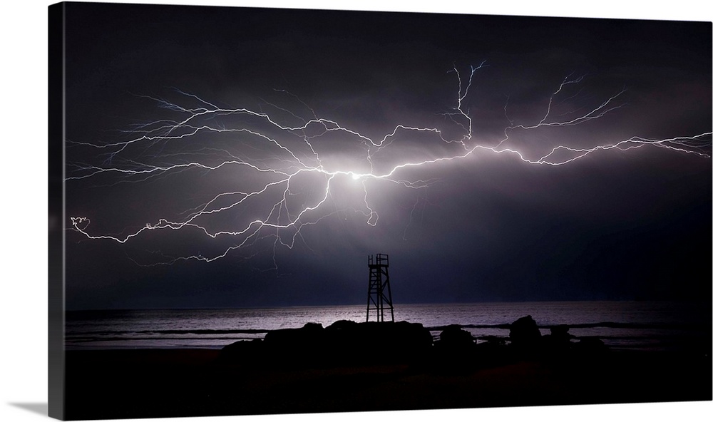 Giant, bright lightning bolt across the sky over a lifeguard tower on the beach by the ocean.