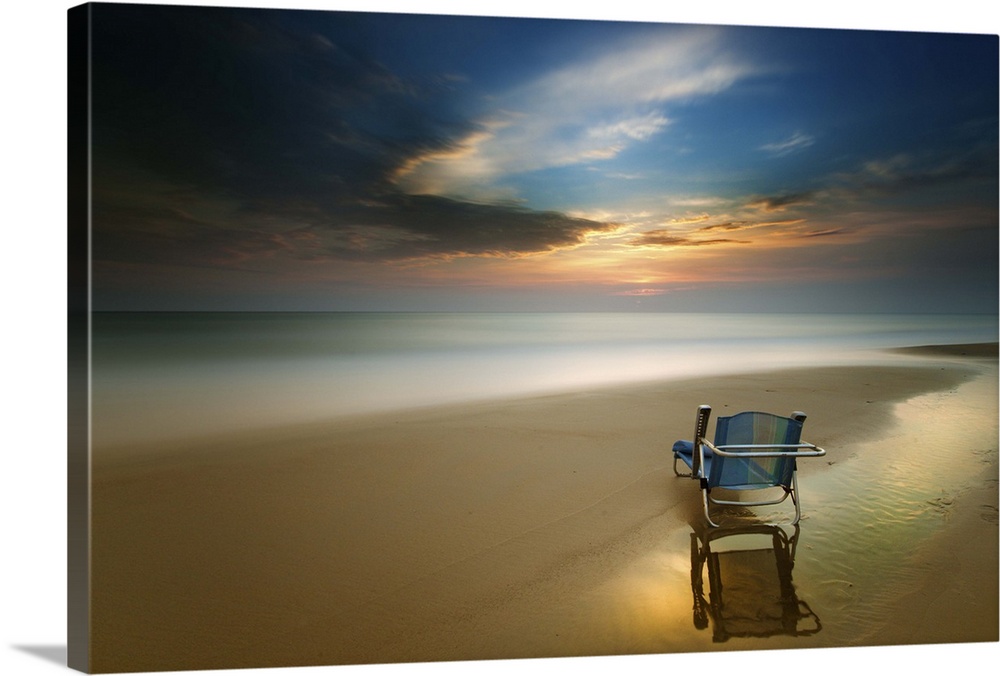 Long exposure seascape photograph of a beach chair on the shore during sunset.