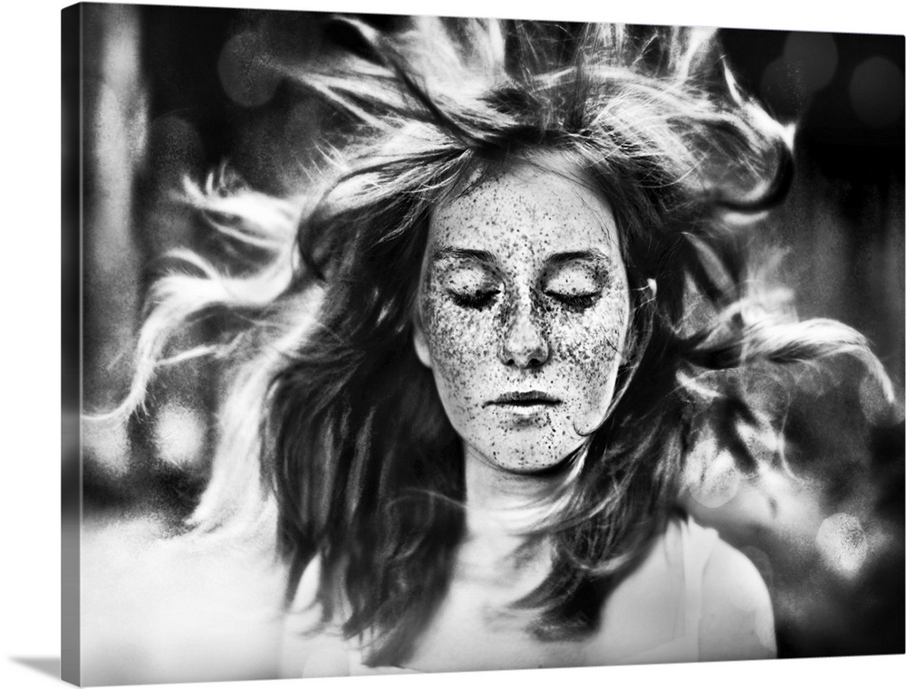 A freckled young woman with closed eyes and her hair blowing in the wind.