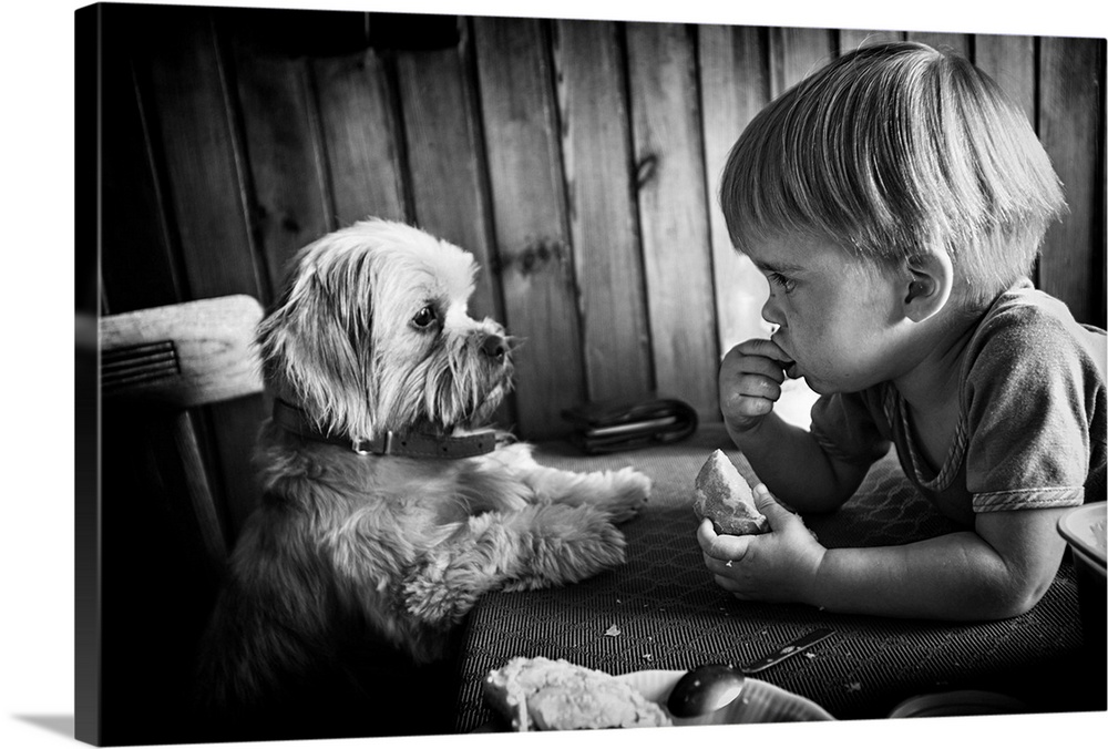 A little boy eats a loaf of bread while a puppy watches intently.
