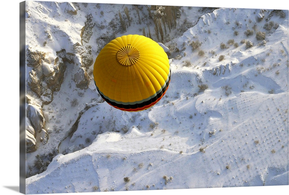 A yellow hot air balloon floats above the snow covered landscape of Cappadocia, Turkey.