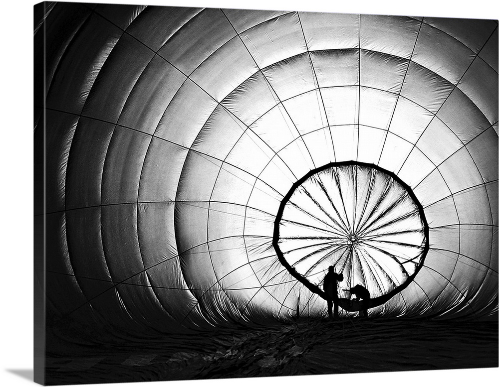 Silhouettes of two figures working on an inflating hot air balloon.