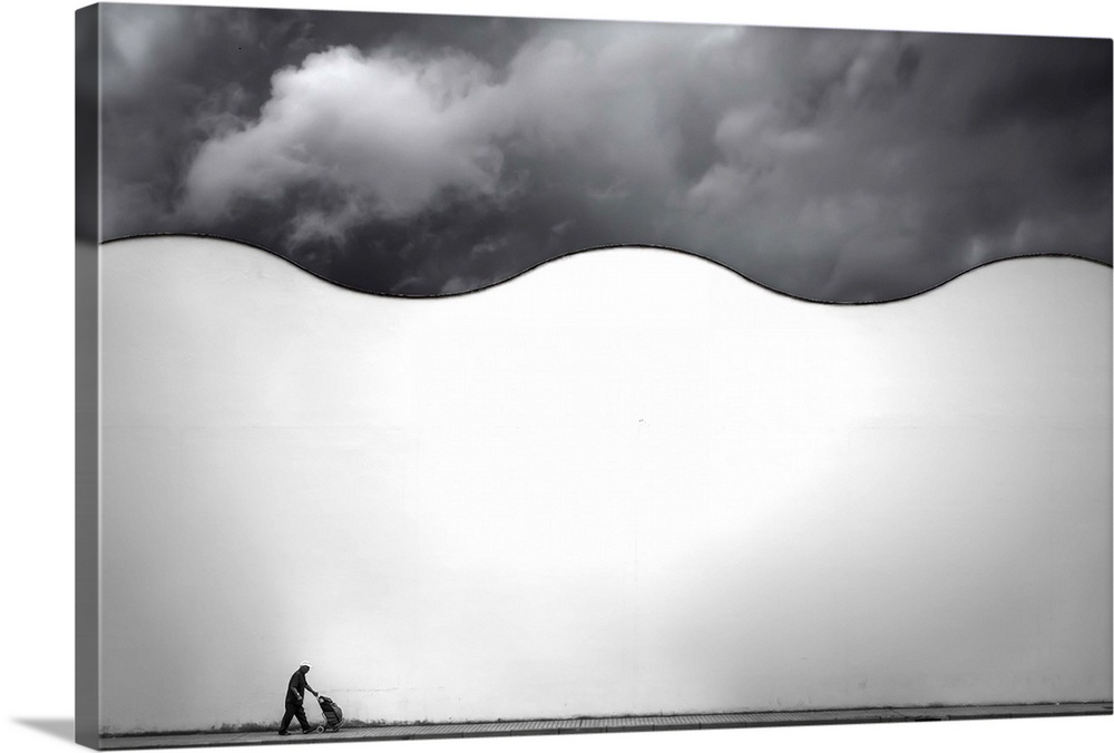 A man walks on a sidewalk below a wavy white wall, on a cloudy day.