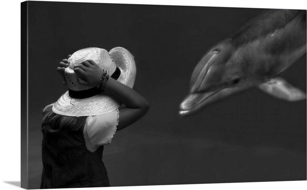 A girl holds her hat in excitement as a captive dolphin swims up to her in an aquarium.