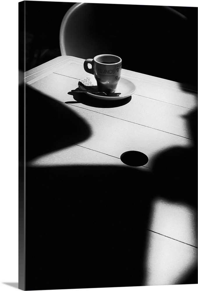 A small coffee cup and saucer sitting on an empty table covered in dark shadows.