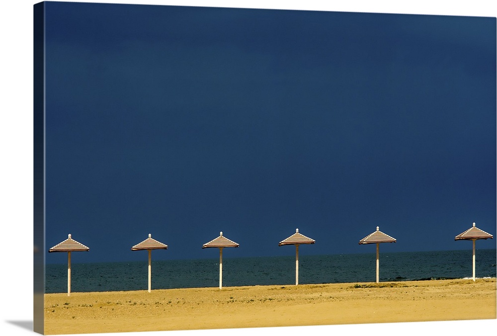 Seascape photograph with a row of red and white striped beach umbrellas awaiting guests.