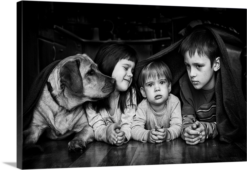 Three siblings and their dog hiding together under a blanket.