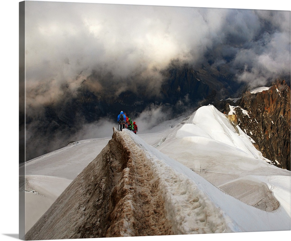 Mountain climbers trekking across a snowy peak on their way to mountains obscured by clouds.